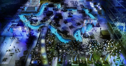 Aerial view of a vibrant pool area at night, featuring illuminated water features and lounge chairs surrounded by palm trees.
