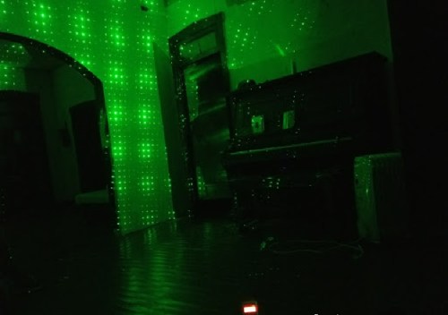 A dimly lit room with green laser lights creating a starry effect on the walls, featuring a piano in the background.