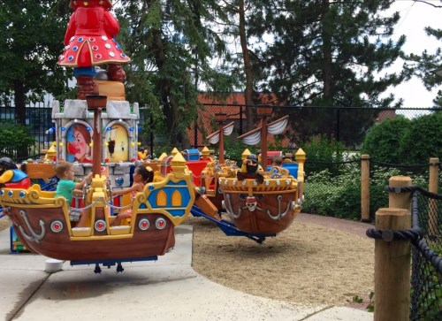 Two colorful pirate ship rides in a playground, with children enjoying the attractions surrounded by greenery.