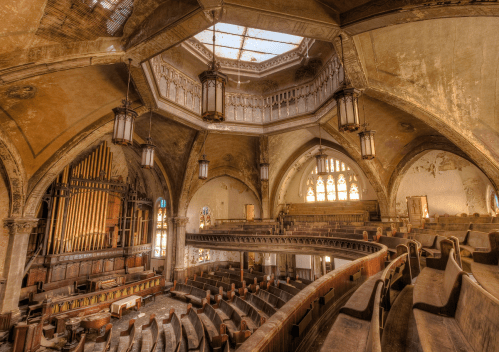 Abandoned church interior with ornate architecture, stained glass windows, and a large pipe organ. Dusty and decaying atmosphere.
