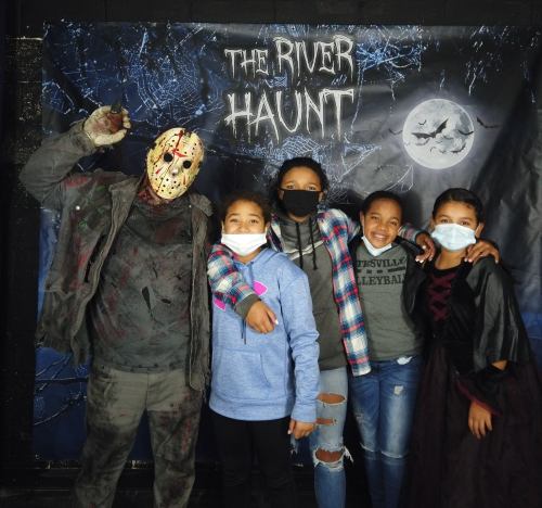 A group of children poses with a person in a horror costume against a spooky backdrop for a Halloween event.