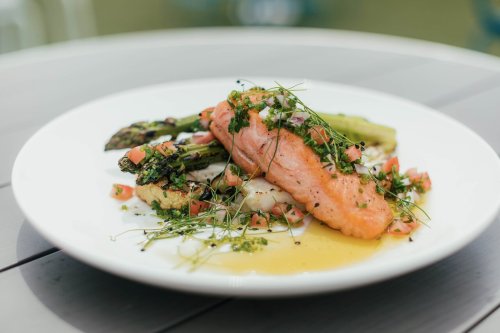 A plate of grilled salmon topped with herbs, served with asparagus and diced tomatoes on a white dish.