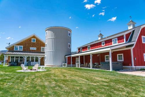 A scenic farm with a red barn, a gray silo, and a spacious lawn under a blue sky with a few clouds.