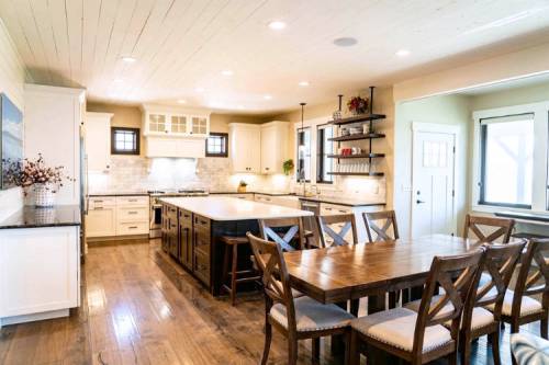 Bright, modern kitchen with white cabinets, a large island, and a wooden dining table, featuring warm wood flooring.