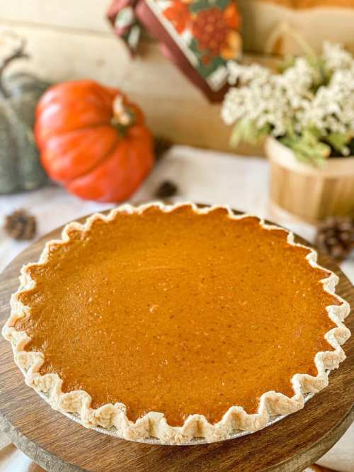 A freshly baked pumpkin pie on a wooden board, with decorative pumpkins and flowers in the background.