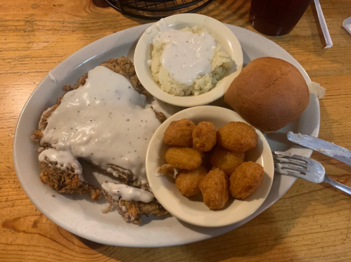A plate of fried chicken smothered in gravy, mashed potatoes with gravy, a roll, and corn fritters.