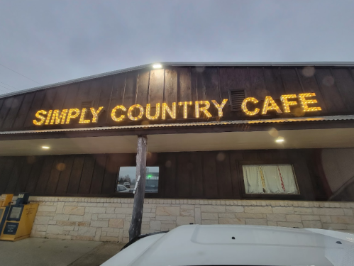 A rustic building with a sign reading "Simply Country Cafe" illuminated by warm lights.