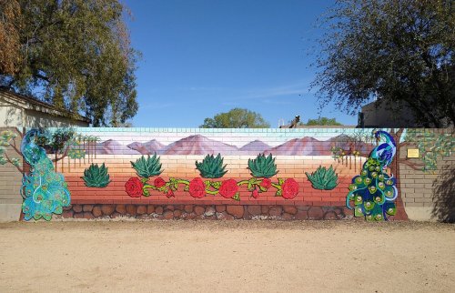 Colorful mural featuring peacocks, cacti, and flowers against a desert landscape with mountains in the background.