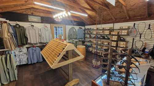 A cozy retail space featuring clothing, fishing gear, and accessories, with wooden displays and a rustic ceiling.