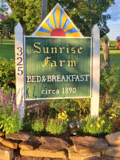 Sign for Sunrise Farm Bed & Breakfast, established in 1890, surrounded by greenery and flowers.