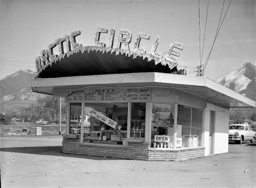 A vintage Arctic Circle fast-food stand with a distinctive sign and menu, set against a mountainous backdrop.