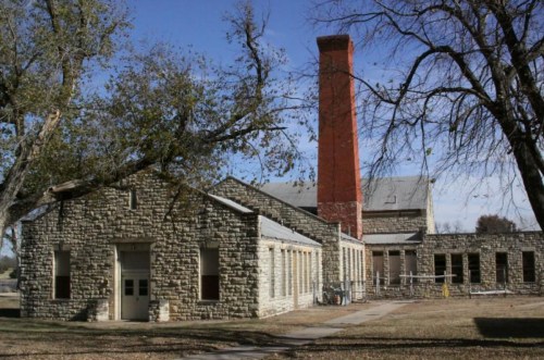 Historic stone building with a tall red chimney, surrounded by trees and a clear blue sky.