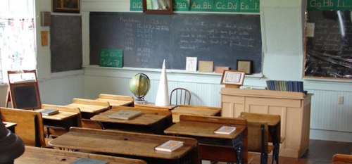 A vintage classroom with wooden desks, a globe, chalkboards, and educational materials on display.