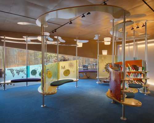 A modern library interior featuring curved shelves, colorful panels, and cozy seating areas. Brightly lit and inviting.