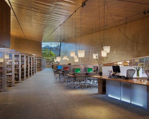 Modern library interior with sleek design, computers, bookshelves, and large windows letting in natural light.