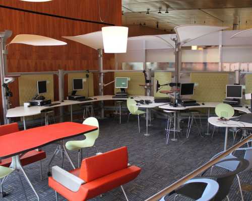 A modern workspace featuring multiple computer stations, colorful chairs, and a bright, open layout.