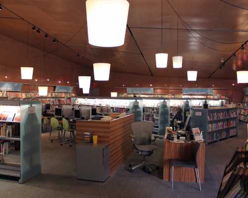 A modern library interior with bookshelves, computers, and pendant lighting, creating a bright and inviting atmosphere.