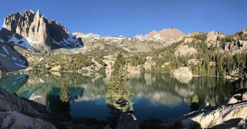 A serene mountain lake surrounded by towering peaks and lush trees, reflecting the clear blue sky.