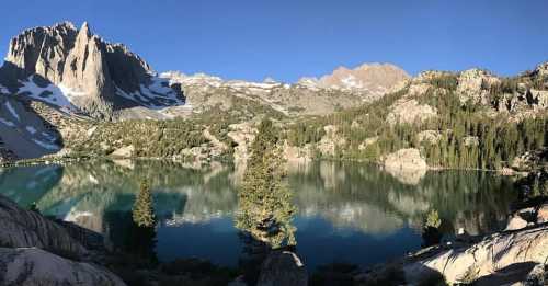 A serene mountain lake surrounded by towering peaks and lush trees, reflecting the clear blue sky.