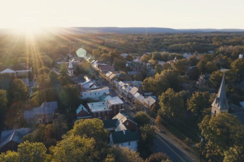 Aerial view of a small town at sunset, with trees, buildings, and a church steeple illuminated by golden light.