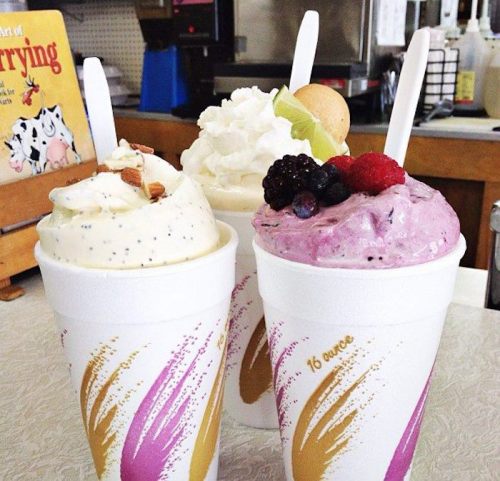 Three cups of colorful ice cream topped with fruit and whipped cream, sitting on a counter in a shop.