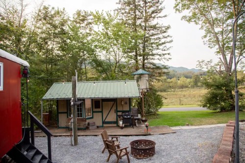 A cozy cabin with a green metal roof surrounded by trees, a fire pit, and a scenic view of the landscape.