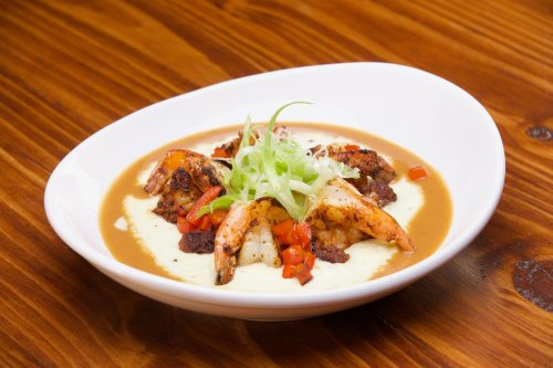 A plate of shrimp served on creamy grits, topped with green onions and diced red peppers, on a wooden table.