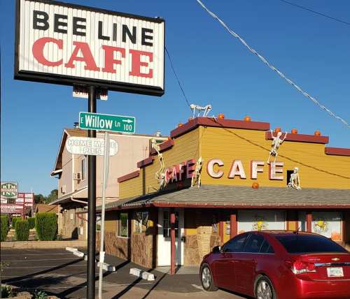 A cafe with a sign reading "Bee Line Cafe," decorated with skeletons and pumpkins, located at the corner of Willow Lane.