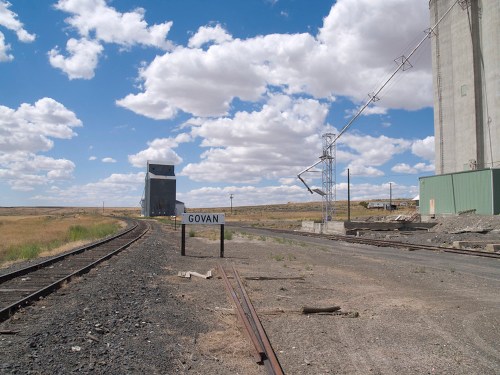 A railway track leads to a grain elevator in Govan, under a blue sky with fluffy clouds.
