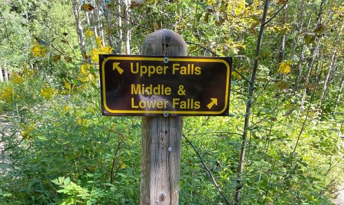 A wooden signpost in a forest, indicating directions to Upper Falls and Middle & Lower Falls.