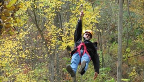 A person in a helmet zip-lining through a forest with colorful autumn leaves.