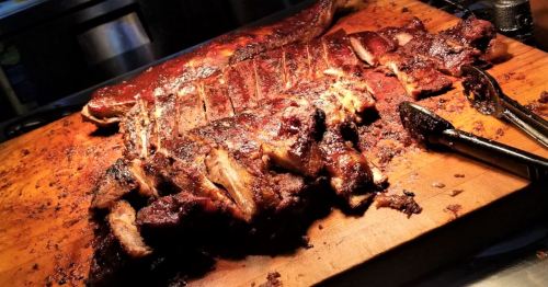 A close-up of a wooden cutting board with succulent, grilled meat, showcasing a rich, smoky glaze and charred edges.