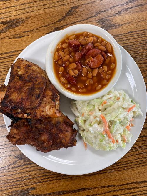A plate with two pieces of fried chicken, a bowl of baked beans with sausage, and a side of coleslaw.