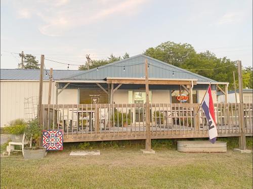 A rustic building with a porch, featuring a sign, plants, and a decorative quilt on the railing.