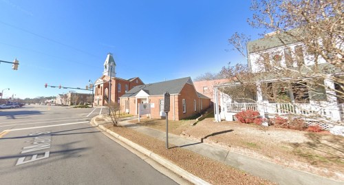 Street view of a small town featuring a church and residential buildings under a clear blue sky.