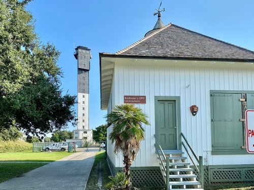 Historic building with a green door and palm tree, next to a tall observation tower against a clear blue sky.