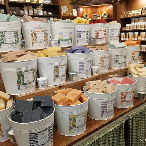 A display of colorful soap bars in buckets, arranged neatly on a wooden shelf in a shop.