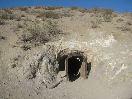 A wooden entrance to a mine tunnel set in a rocky, arid landscape with sparse vegetation.