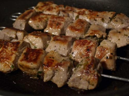 Grilled skewers of marinated meat, golden brown and sizzling in a pan.