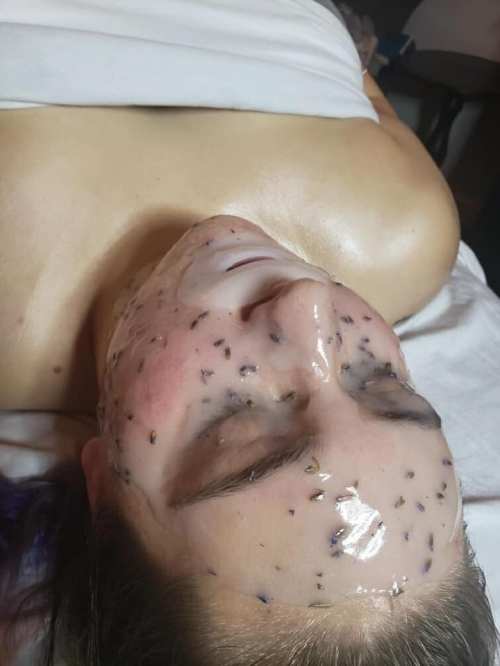 A person lying down with a gel-like mask on their face, dotted with small dark particles.
