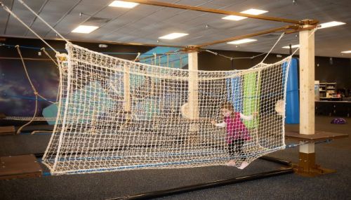 A child plays on a rope net structure in a colorful indoor play area.
