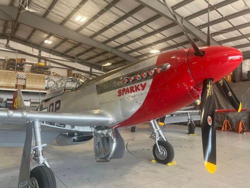 A vintage silver and red airplane named "Sparky" inside a hangar, showcasing its propeller and sleek design.