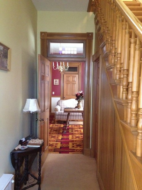 A hallway with wooden walls, a staircase, and a view into a cozy living room with a chandelier and floral decor.