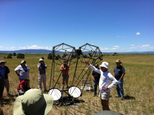 A group of people in a field, gathered around a large structure, with one person pointing and explaining something.