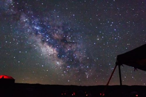 A stunning view of the Milky Way galaxy filled with stars, with a dark landscape silhouette in the foreground.