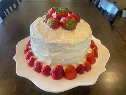 A layered cake topped with fresh strawberries and surrounded by more strawberries on a white plate.