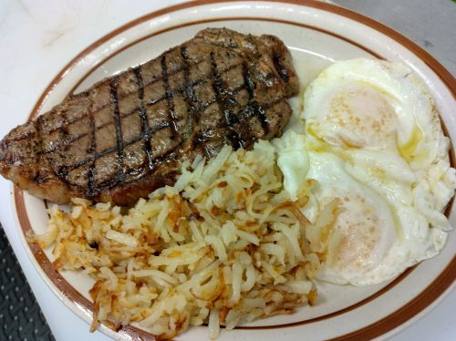 A plate with a grilled steak, two fried eggs, and crispy hash browns.