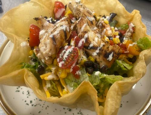 A colorful salad with grilled chicken, tomatoes, corn, and black beans served in a crispy tortilla bowl.