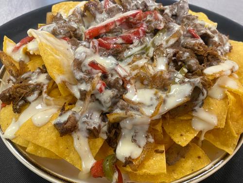 A plate of nachos topped with shredded beef, melted cheese, and colorful peppers.