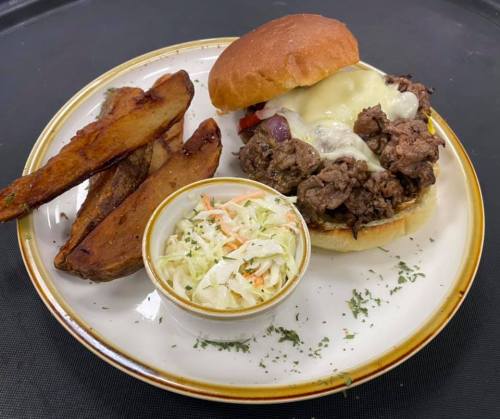 A hearty sandwich filled with beef and melted cheese, served with potato wedges and a side of coleslaw.